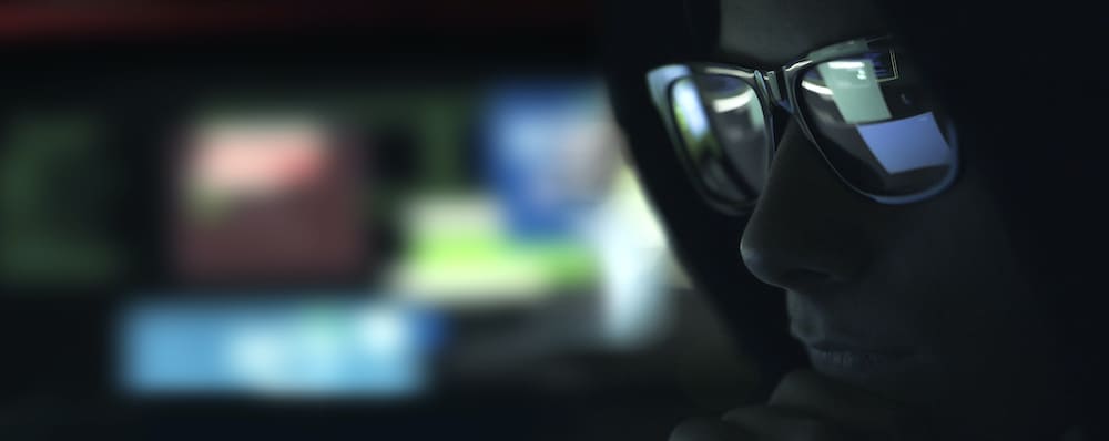  A hacker with glasses working with a computer in the dark.