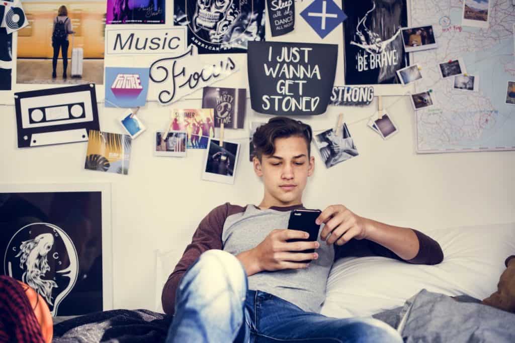 A teenager on his phone in his room with a multitude of posters in Calgary. 