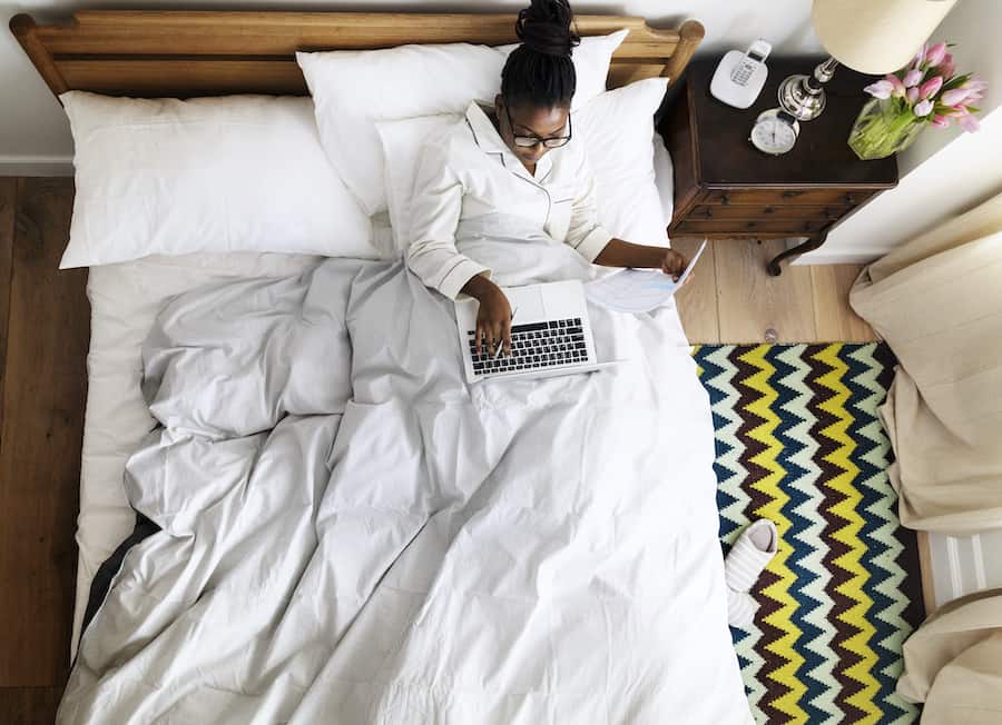 A woman working on a computer from her bed due to the extensive It Services in Calgary. 